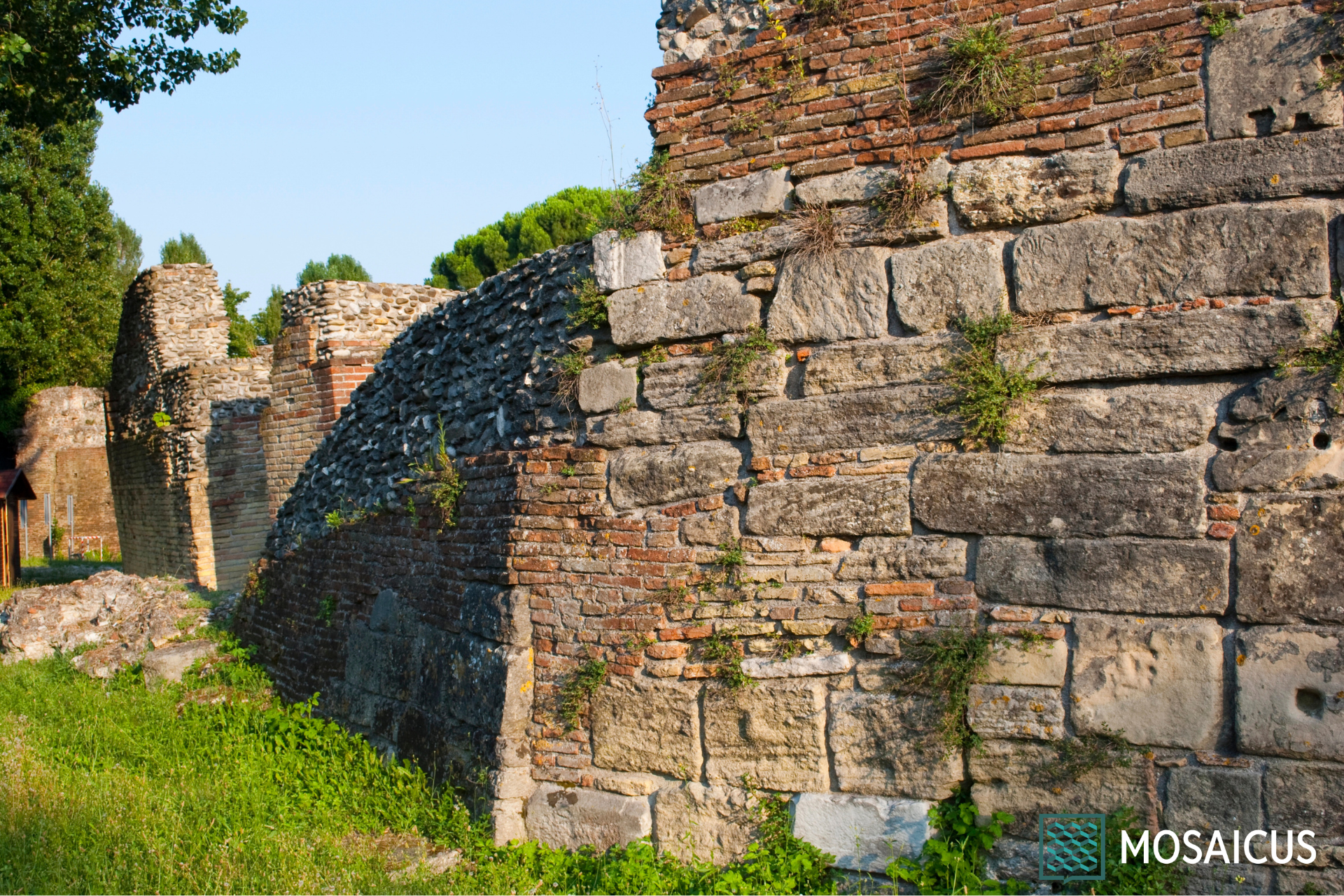 Il nostro percorso inizia dall’Arco d’Augusto, eretto nel 27 a.C. per celebrare il restauro delle strade voluto dall’imperatore; si tratta della porta urbica più antica e meglio conservata dell’Italia settentrionale. Realizzato in pietra d’Istria, l’Arco è ingentilito con clipei e capitelli corinzi, tra cui si possono riconoscere le divinità protettrici Giove, Apollo, Nettuno e la dea Roma. L’area circostante mostra tracce delle antiche mura romane e, proseguendo lungo l’antico decumano massimo, oggi Corso d’Augusto, si giunge in Piazza Tre Martiri, l’area in cui sorgeva il Foro Romano, fulcro della vita politica ed economica. Qui, secondo la tradizione, Giulio Cesare rivolse il celebre discorso alle legioni dopo aver varcato il Rubicone nel 49 a.C., evento commemorato da un cippo rinascimentale e da una statua bronzea di Augusto. Poco distante, all’estremità del cardo massimo, possiamo ancora ammirare la Porta Montanara, antico varco d’accesso per chi proveniva dalla valle del Marecchia e dai rilievi appenninici. Visiteremo poi la straordinaria area archeologica della Domus del Chirurgo, una ricca dimora del II secolo d.C. dove è stato rinvenuto il più completo corredo chirurgico del mondo antico, composto da circa 150 strumenti, oggi custoditi nel vicino Museo della Città. Attraverseremo poi il Ponte di Tiberio, imponente opera ingegneristica in pietra d’Istria completata nel 21 d.C., che con le sue cinque arcate segna idealmente l’inizio della Via Emilia verso Piacenza e della Via Popilia verso Ravenna. La visita guidata alla Rimini romana si conclude con l’Anfiteatro Romano, capace un tempo di ospitare oltre 12.000 spettatori per i combattimenti gladiatori e costruito nel II secolo d.C. su volere di Adriano, in una scenografica posizione a pochi passi dal mare.